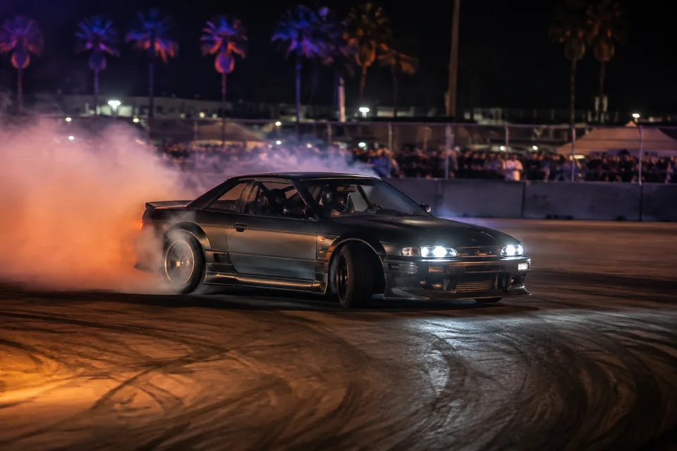 A drift car countersteering through tire smoke at night